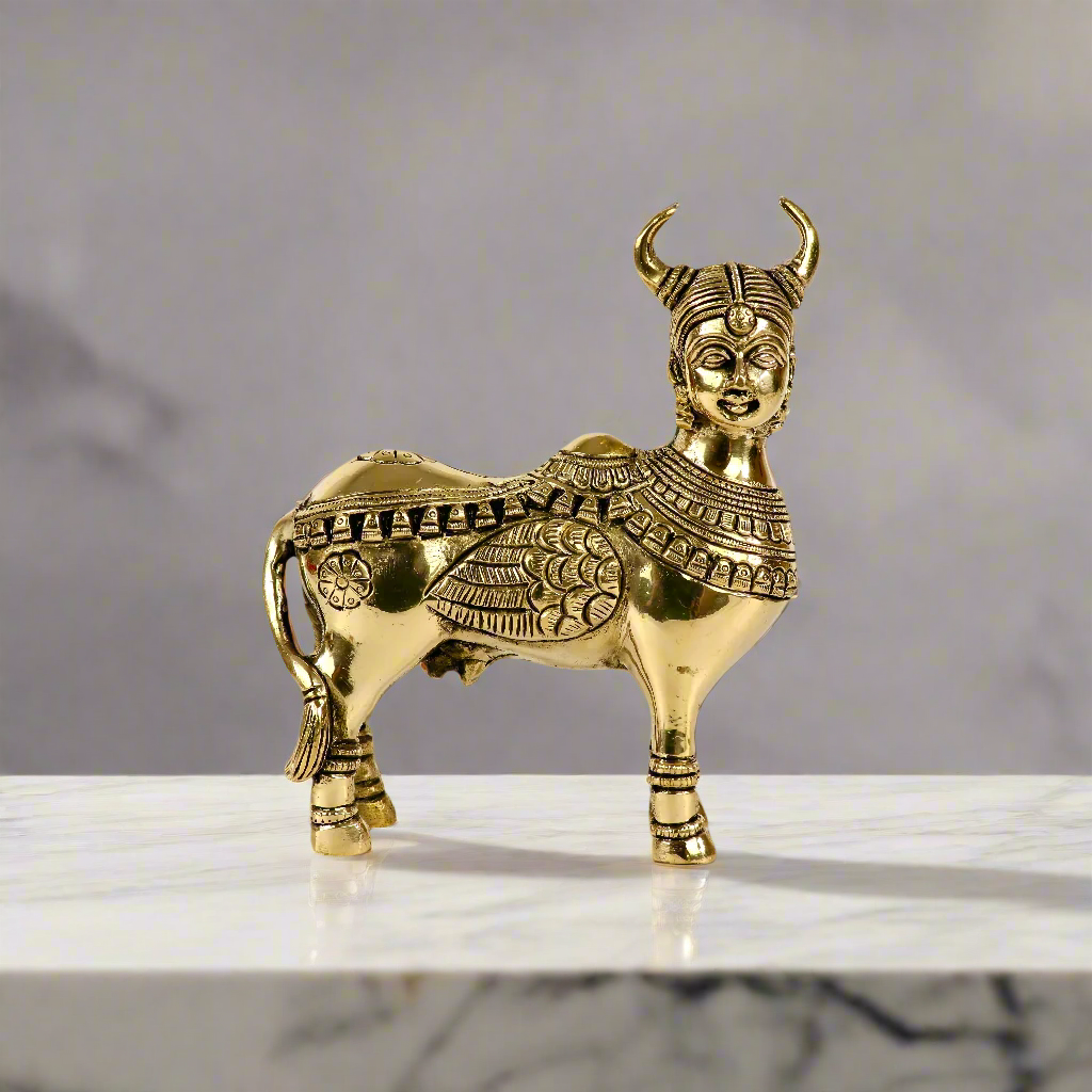 Product image of a Brass Kamdhenu Cow from Indian Impressions, intricately crafted with detailed carvings. The cow is depicted in a standing posture, symbolizing prosperity, abundance, and spiritual significance. Finished in polished brass, this piece is ideal for Vastu, spiritual practices, home décor, or gifting to bring positive energy and blessings to any space.