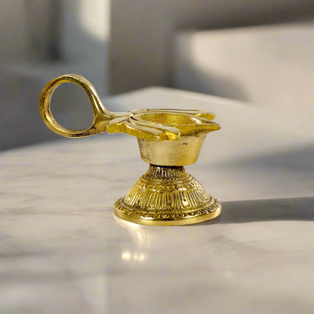 Product image of a Brass Lotus Diya with Handle from Indian Impressions, featuring a beautifully crafted lotus design and a sturdy handle for ease of use. Made from polished brass, this diya is ideal for Vastu, spiritual rituals, home décor, or gifting, symbolizing purity, positivity, and divine light.