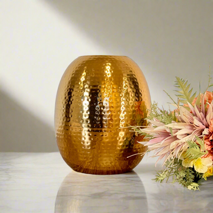 Product image of the Oval Vase Hammered Gold from Indian Impressions, featuring a sleek oval design with a textured hammered finish. Crafted with a polished gold-tone, this vase is perfect for displaying flowers or as a standalone décor piece. Ideal for Vastu, home décor, or gifting, adding elegance and sophistication to any space.