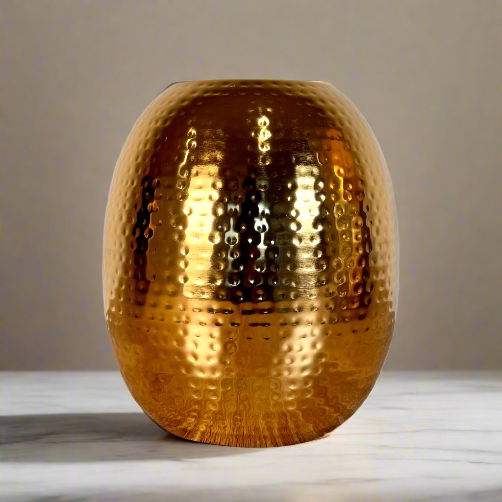 Product image of the Oval Vase Hammered Gold from Indian Impressions, featuring a sleek oval design with a textured hammered finish. Crafted with a polished gold-tone, this vase is perfect for displaying flowers or as a standalone décor piece. Ideal for Vastu, home décor, or gifting, adding elegance and sophistication to any space.